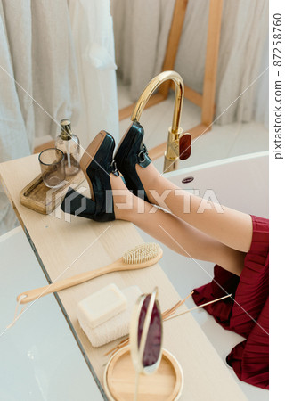 Photo of a womens legs in black high-heeled shoes with a buckle in a bath Photo of a womens legs in black high-heeled shoes with a buckle in a bath 87258760
