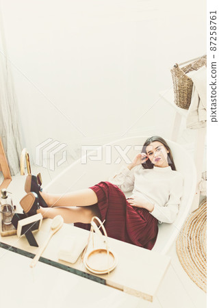 Portrait of fashionable women in red skirt, white blouse and stylish beige high-heeled shoes with a chain buckle posing in a bed Portrait of fashionable women in red skirt, white blouse and stylish beige high-heeled shoes with a chain buckle posing in a bed 87258761