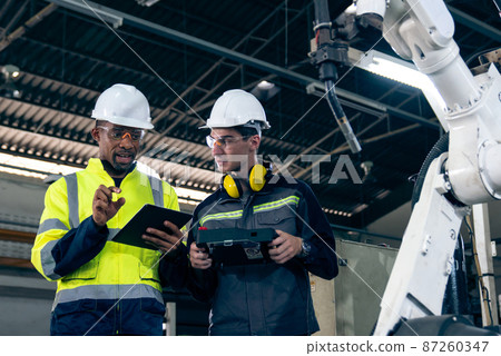 Factory workers working with adept robotic arm in a workshop 87260347