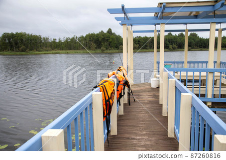 Orange life jackets and fishing equipment on the fishing bridge. The concept of safety behavior on the water, accident, drowning of a person. Copy space for text 87260816