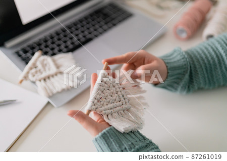 Hand of a woman when she is making macrame. Natural cotton threads and wooden beads. Handmade macrame belt in work process. Female hobby. 87261019