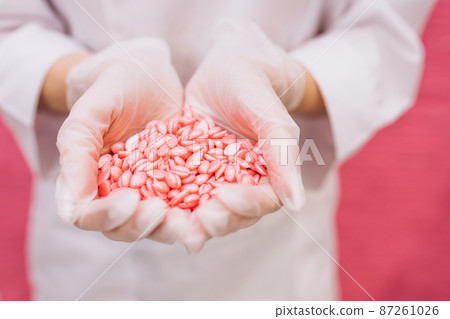 Wax for depilation of pink color in the form of a heart. The concept of depilation, waxing, smooth skin. Copy space, banner, flyer. Hard wax beans in woman palms 87261026