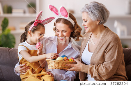 Happy family in bunny ears laugh and play with eggs at home during preparation for Easter holiday 87262204