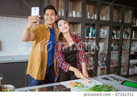 asian couple taking selfie while cooking together in the kitchen 87262352