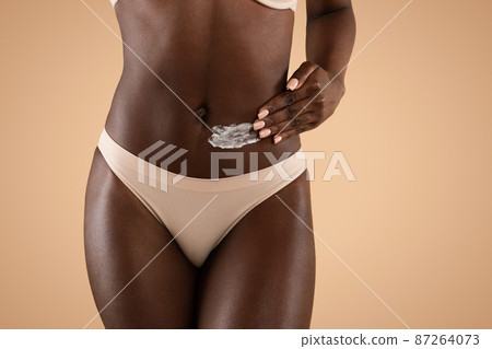 Cropped of dark-skinned woman applying cream on her waist Cropped of dark-skinned woman applying cream on her waist 87264073