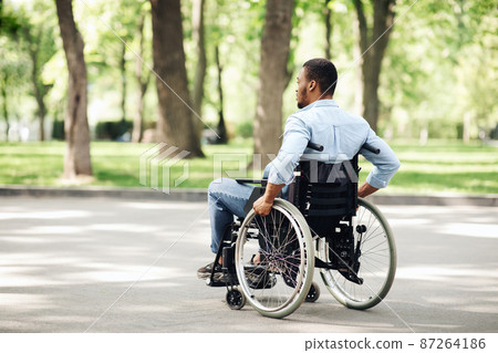 Thoughtful young black guy in wheelchair having walk at urban park, copy space 87264186