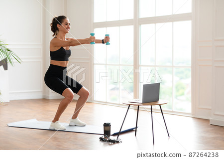 Young woman exercising with dumbbells in front of laptop 87264238