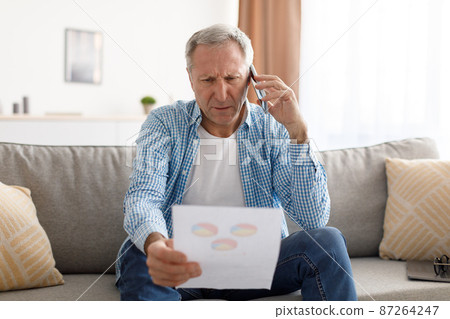 Focused mature man holding paper reading report talking on phone Focused mature man holding paper reading report talking on phone 87264247