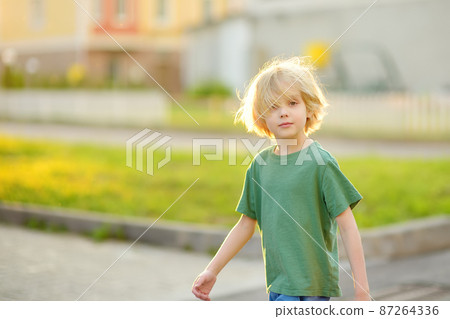 Cheerful little boy enjoying warm sunny summer day of holidays. Active child playing on the street of small town. Freedom, rest, vacation and childhood concept. Cheerful little boy enjoying warm sunny summer day of holidays. Active child playing on the street of small town. Freedom, rest, vacation and childhood concept. 87264336