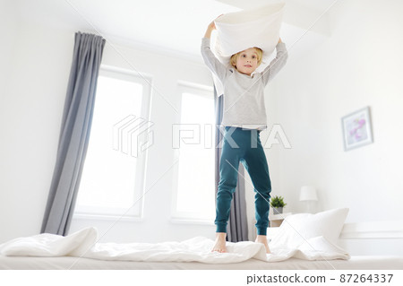 Happy little boy in pajamas jumps on his parents bed in the morning. A happy childhood for kids with a loving family. Happy little boy in pajamas jumps on his parents bed in the morning. A happy childhood for kids with a loving family. 87264337