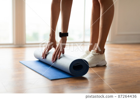 Closeup of young woman unrolling yoga mat on floor 87264436