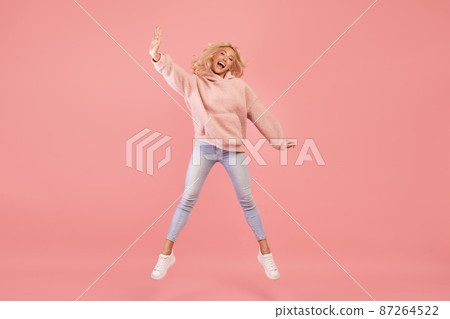 Expressing joy and happiness. Full length shot of active young woman jumping and having fun over pink background Expressing joy and happiness. Full length shot of active young woman jumping and having fun over pink background 87264522