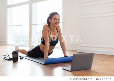 Young woman stretching back on mat with pc Young woman stretching back on mat with pc 87264526