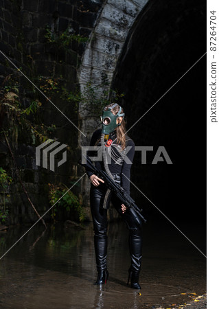 A woman in a black suit and gas mask with a machine gun in her hands A woman in a black suit and gas mask with a machine gun in her hands 87264704