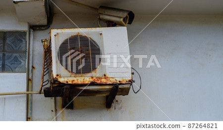 Rust air conditioner machine outdoor unit mounted onto the wall. weathered and abandoned unit close-up shot. 87264821