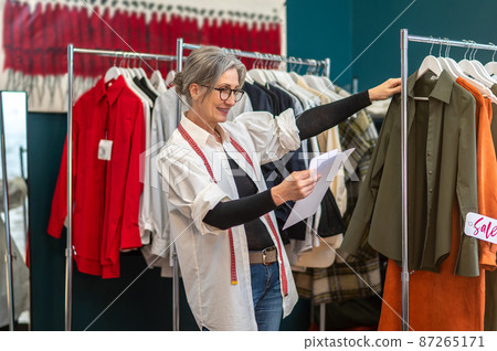 Woman looking at sketch touching hanging blouse Woman looking at sketch touching hanging blouse 87265171