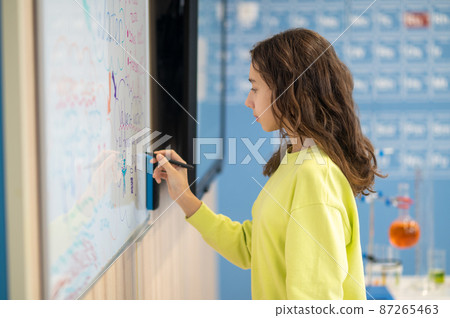 Girl standing sideways to camera writing on board Girl standing sideways to camera writing on board 87265463