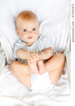 Cute little newborn girl with smiling face looking at camera on white background. Infant baby resting playing lying down on crib bed at home. Motherhood happy child concept Cute little newborn girl with smiling face looking at camera on white background. Infant baby resting playing lying down on crib bed at home. Motherhood happy child concept 87265971