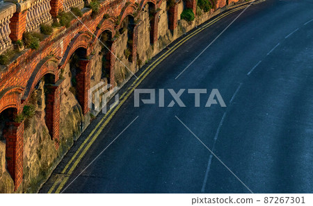 Red brick arches over a black tarmac road 87267301
