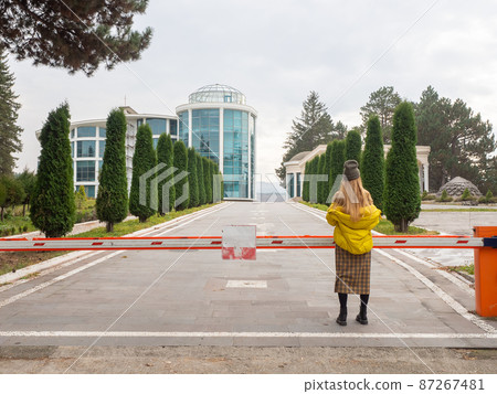 A woman stands at the barrier blocking the path to the alley leading to the modern building in the park 87267481