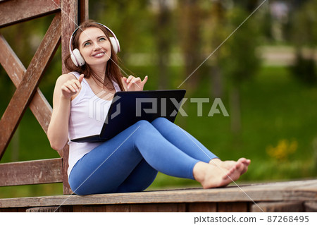 Woman in cordless headphones listens to music outdoors. Woman in cordless headphones listens to music outdoors. 87268495