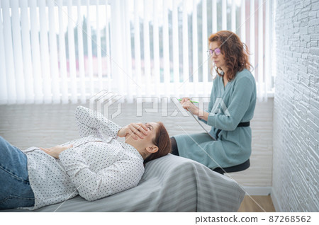 Caucasian woman crying while lying on the couch at a session with a psychologist. 87268562