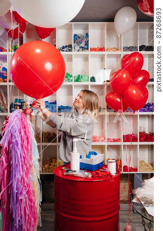 a woman inflates of helium from a big red balloon. 87268693