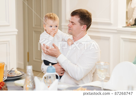 a dark-haired man holds a one-year-old boy in her arms at the banquet.  87268747