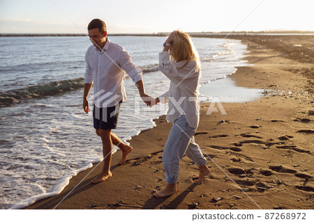 Beautiful couple walking barefoot on the beach holding hands Beautiful couple walking barefoot on the beach holding hands 87268972