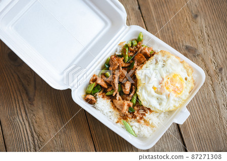 Stir fried pork with red curry paste and basil leaves with yardlong bean and fried egg topped in a plastic box, Thai street food or food delivery 87271308