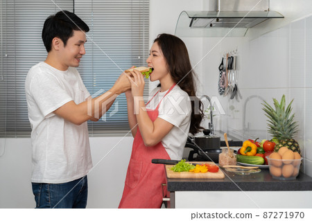 man feeding sandwich to his wife in the kitchen at home man feeding sandwich to his wife in the kitchen at home 87271970