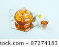 Herbal tea. Transparent glass teapot, cups of tea with orange flowers of calendula on a blue background. Calming drink concept 87274183