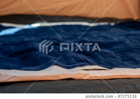 Selective focus of an inflatable air mattress on the floor of a tent being filled up.  87275138