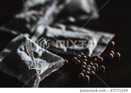 packets of desiccant scattered on a dark surface 87275204