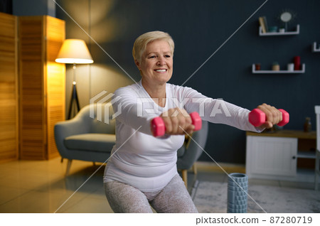 Senior woman training with dumbbells at home Senior woman training with dumbbells at home 87280719