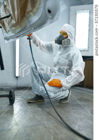 Technician in safety clothing spraying car paint 87280876