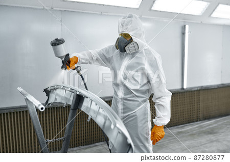 Technician in safety clothing spraying car paint Technician in safety clothing spraying car paint 87280877
