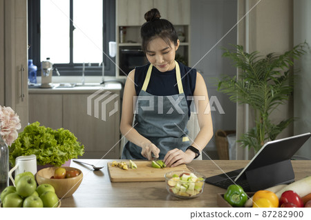 Young woman making fresh healthy vegan salad according a recipe on a tablet. 87282900