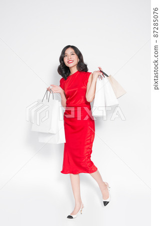 Full length of cheerful fashionable asian woman wearing a red dress with shopping bags 87285076