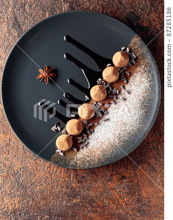 Chocolate truffles on a black plate with chocolate sauce. 87285186