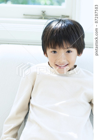 一個微笑的男孩坐在沙發上 87287583