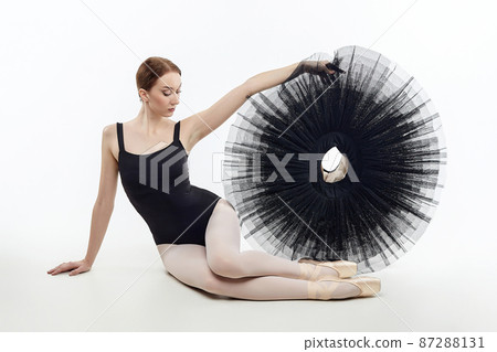 attractive ballerina sits and holds a tutu in her hands. studio photo shoot on a white background 87288131