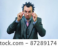 A man with disheveled hair in a business suit adjusts his glasses 87289174