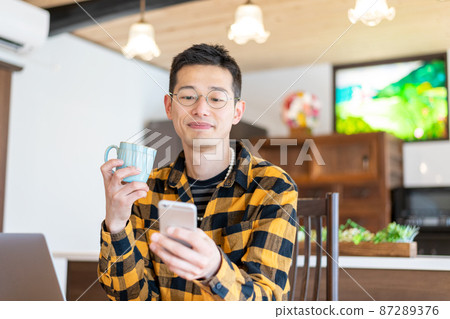 A male entrepreneur who smiles when contacted by a smartphone while working on a PC A male entrepreneur who smiles when contacted by a smartphone while working on a PC 87289376