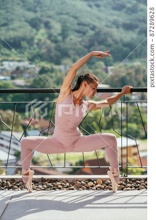 Young fit ballerina in pink pointes stretching standing on toes in warm sunrays Young fit ballerina in pink pointes stretching standing on toes in warm sunrays 87289628