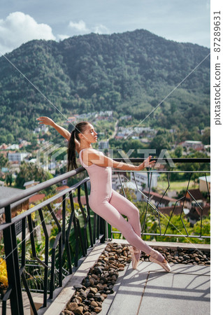 Young fit ballerina pink pointes dancing on toes against mountainous landscape Young fit ballerina pink pointes dancing on toes against mountainous landscape 87289631