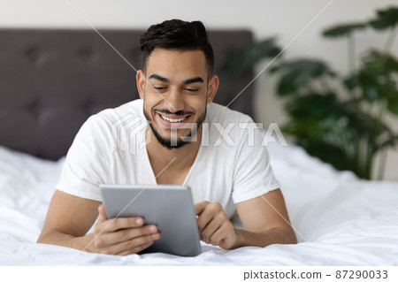 Handsome Arab Guy Browsing Internet On Digital Tablet While Relaxing In Bed 87290033