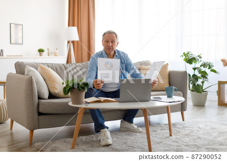 Man holding paper reading report working on laptop at home Man holding paper reading report working on laptop at home 87290052