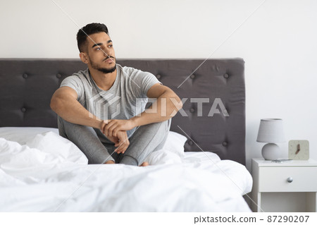 Portrait Of Thoughtful Young Arab Man Sitting On Bed And Looking Away Portrait Of Thoughtful Young Arab Man Sitting On Bed And Looking Away 87290207