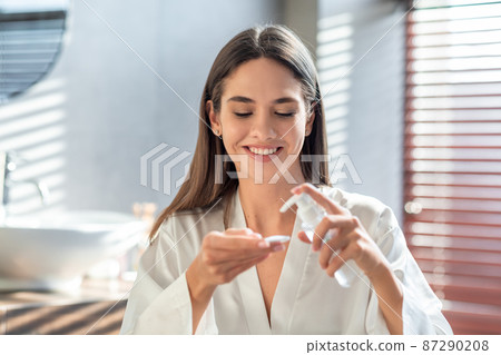 Happy young lady applying hydrophilic oil on cotton pad for cleansing face Happy young lady applying hydrophilic oil on cotton pad for cleansing face 87290208